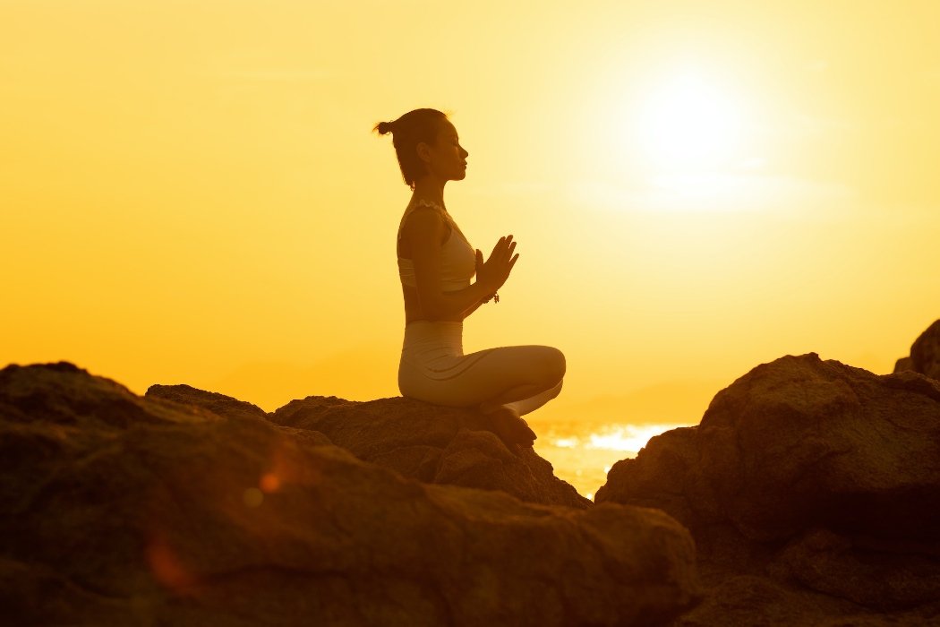 Une femme fait de la méditation face à un coucher de soleil