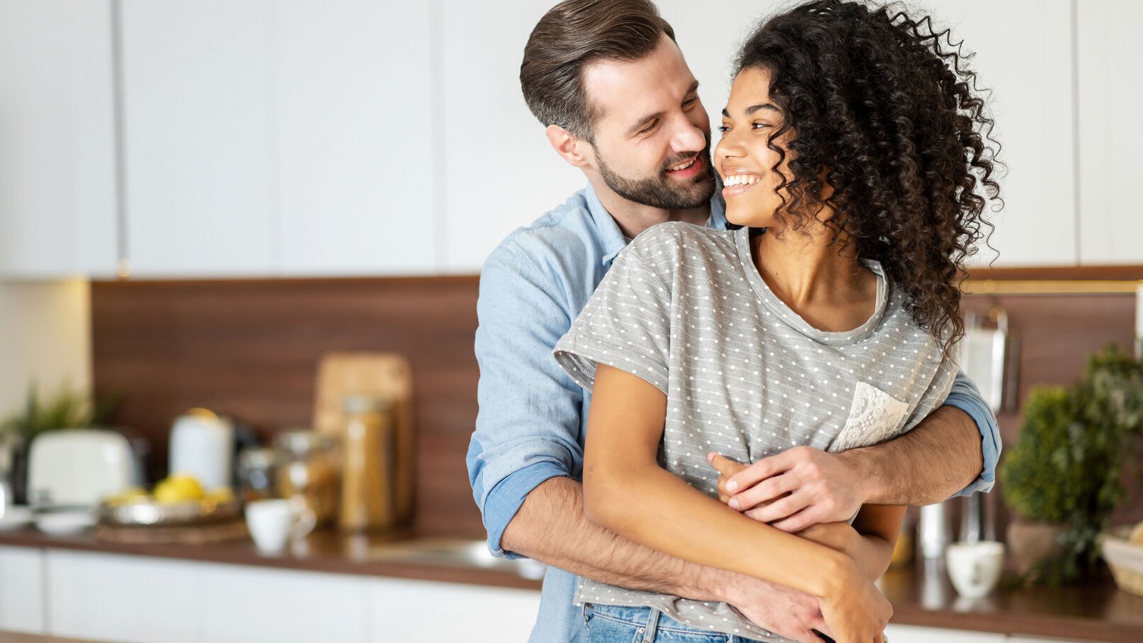 Un couple s’enlace et se sourit dans une cuisine